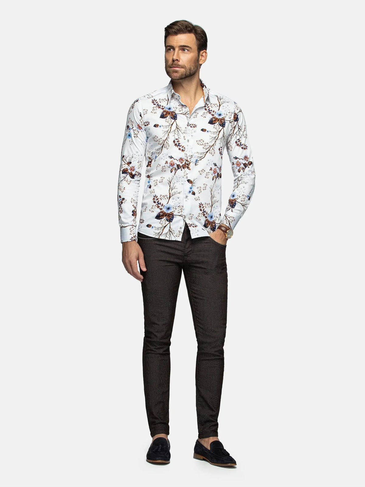 Man wearing a patterned shirt and dark pants on a white background