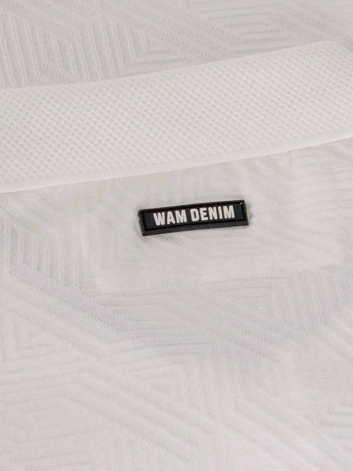 Close-up of the Wam Denim logo on the white polo shirt collar – Wam Denim.