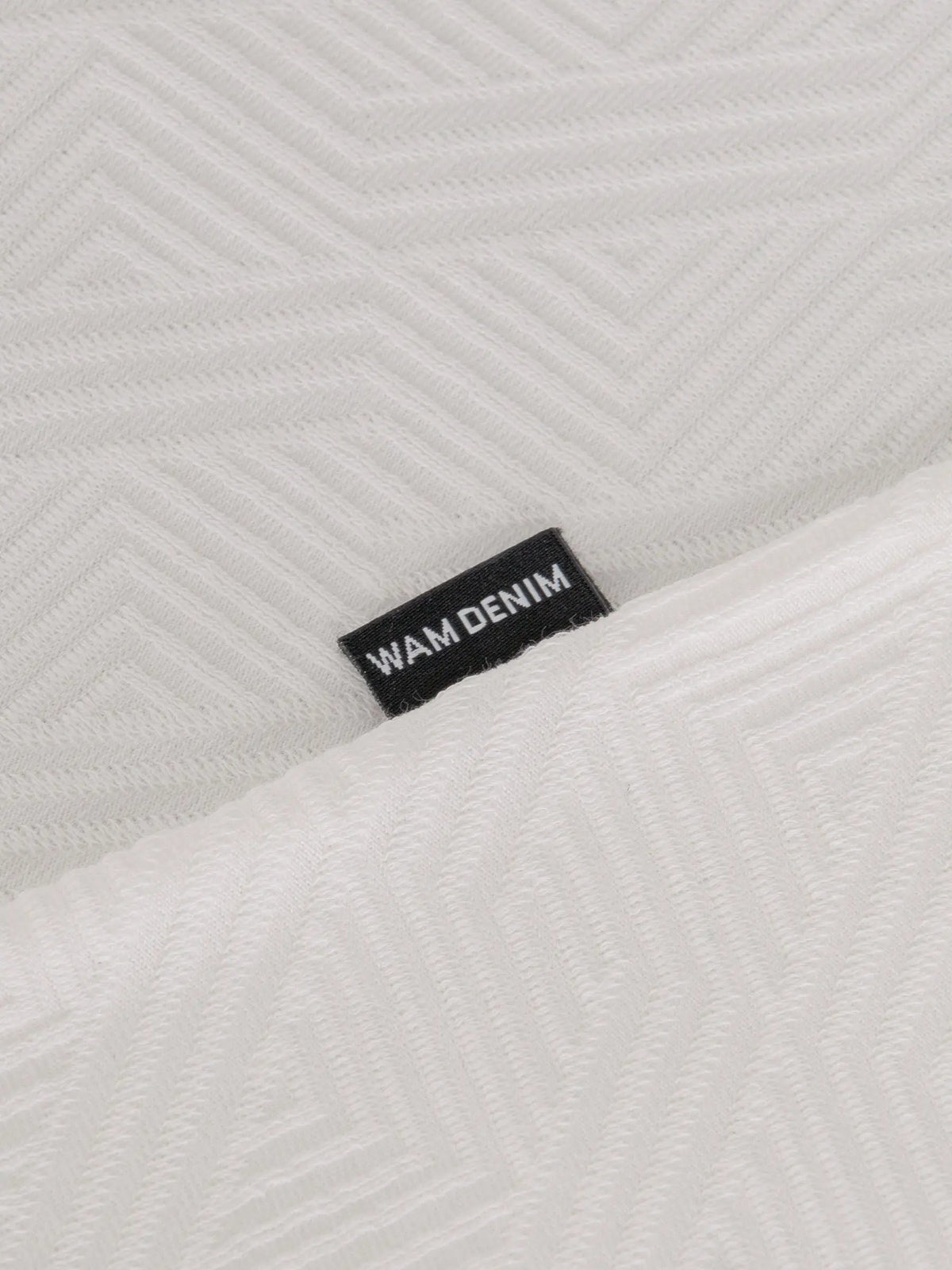 Close-up of the Wam Denim label on the textured white polo – Wam Denim.