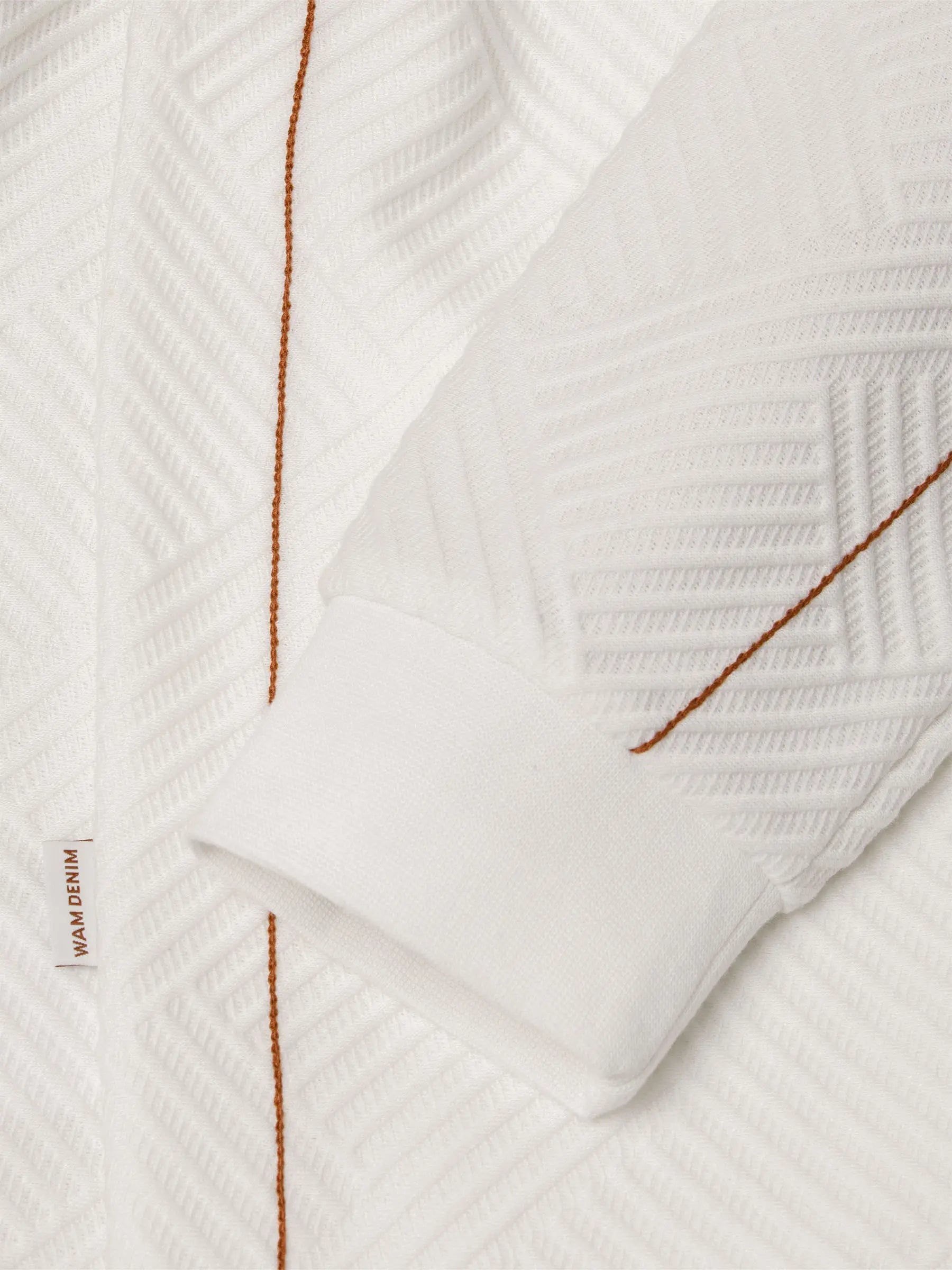 Close-up of white textured sweatshirt sleeve with brown stitching and cuff detail – Wam Denim.