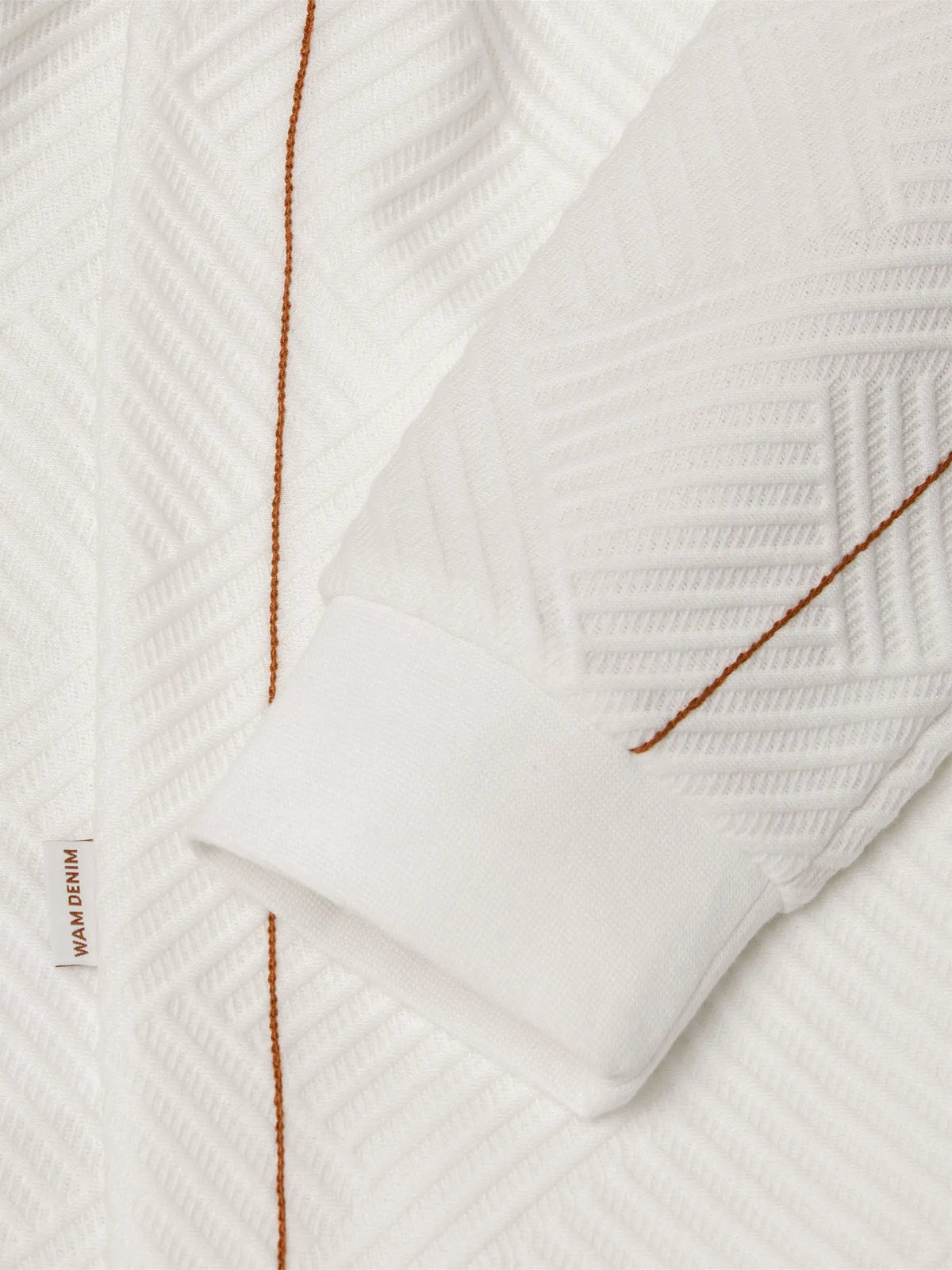 Close-up of white textured sweatshirt sleeve with brown stitching and cuff detail – Wam Denim.