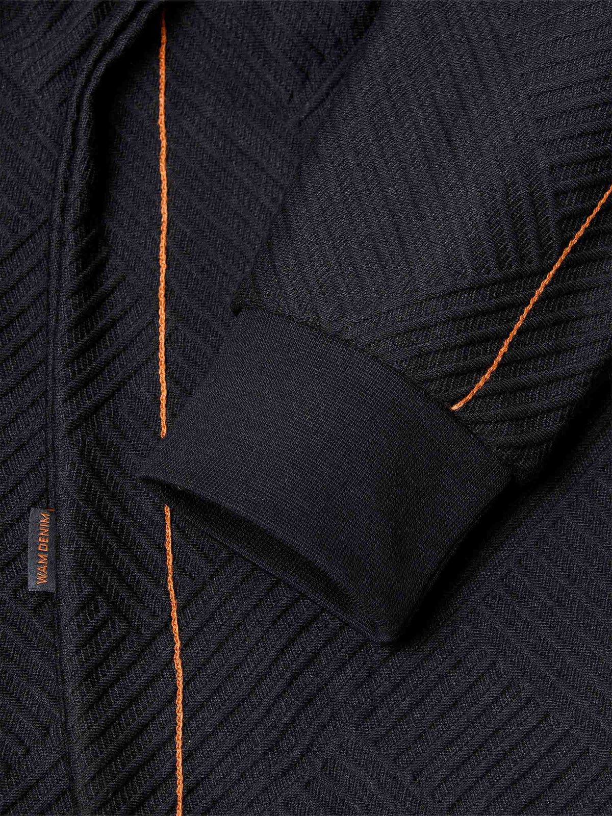 Close-up of sleeve and orange stitch detailing on black textured fabric – Wam Denim.