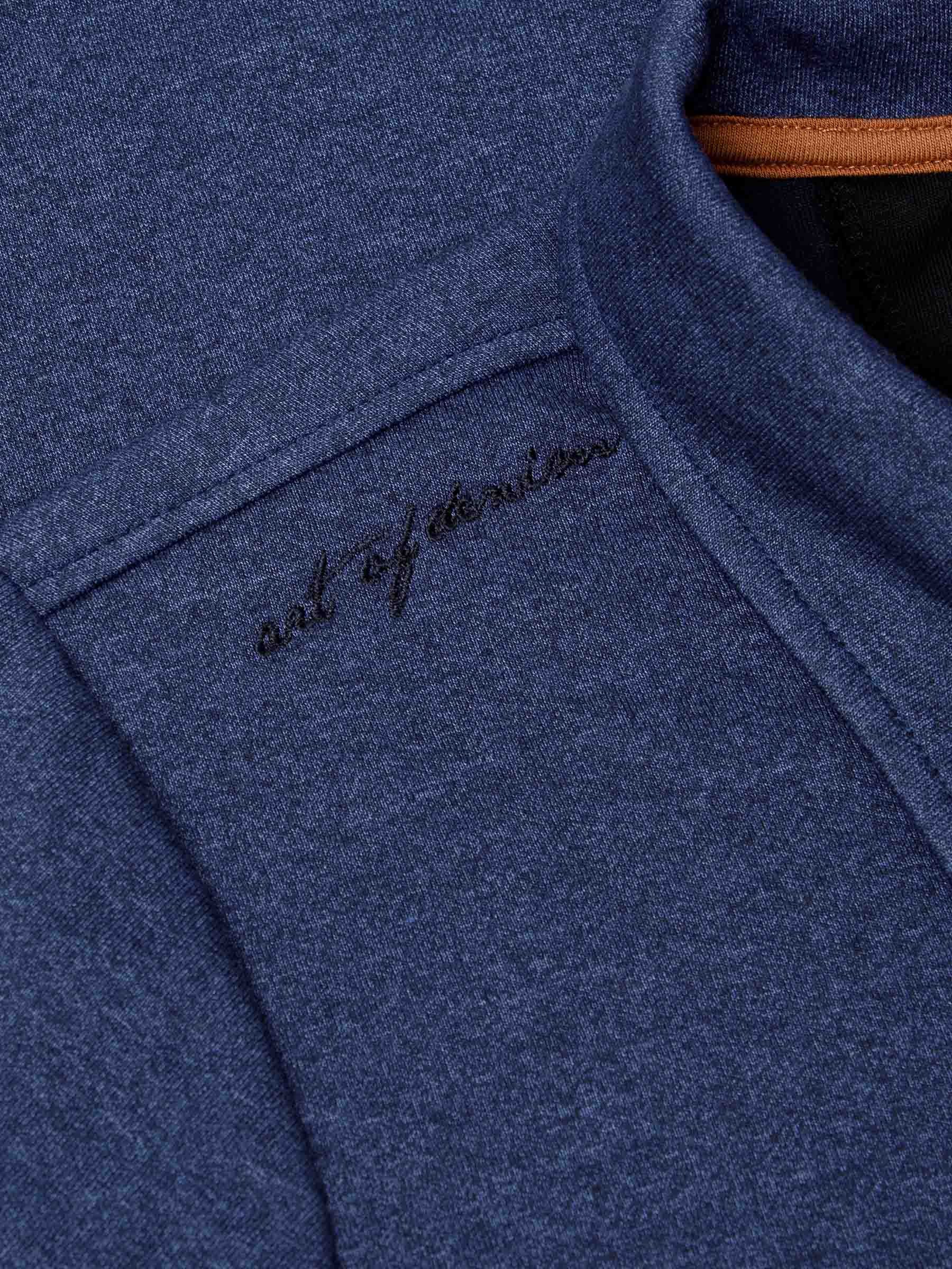 Close-up of embroidered “art of denim” detail on light indigo fabric near collar – Wam Denim.