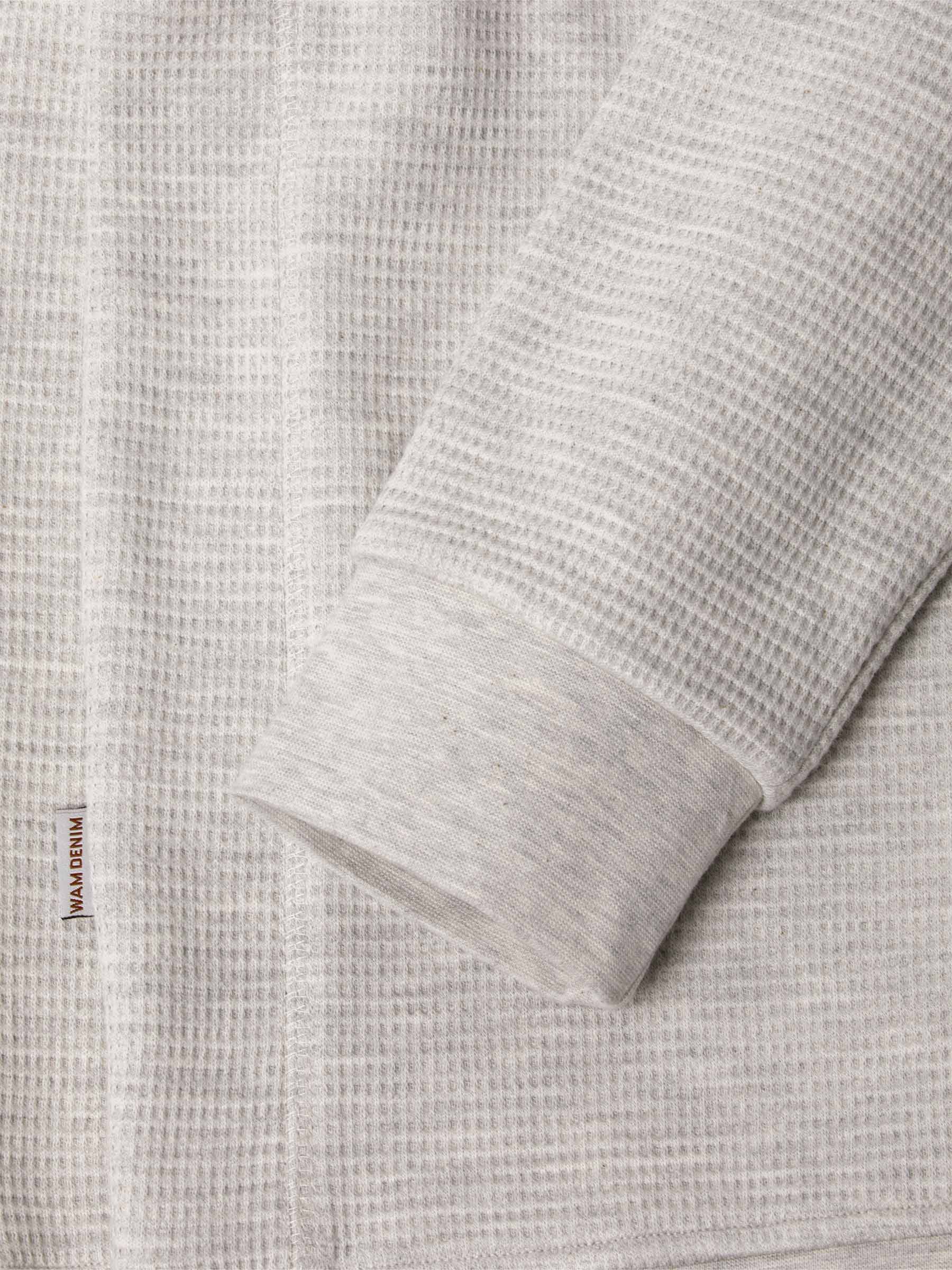 Close-up of light grey waffle-textured sweatshirt sleeve and hem with logo tag – Wam Denim.