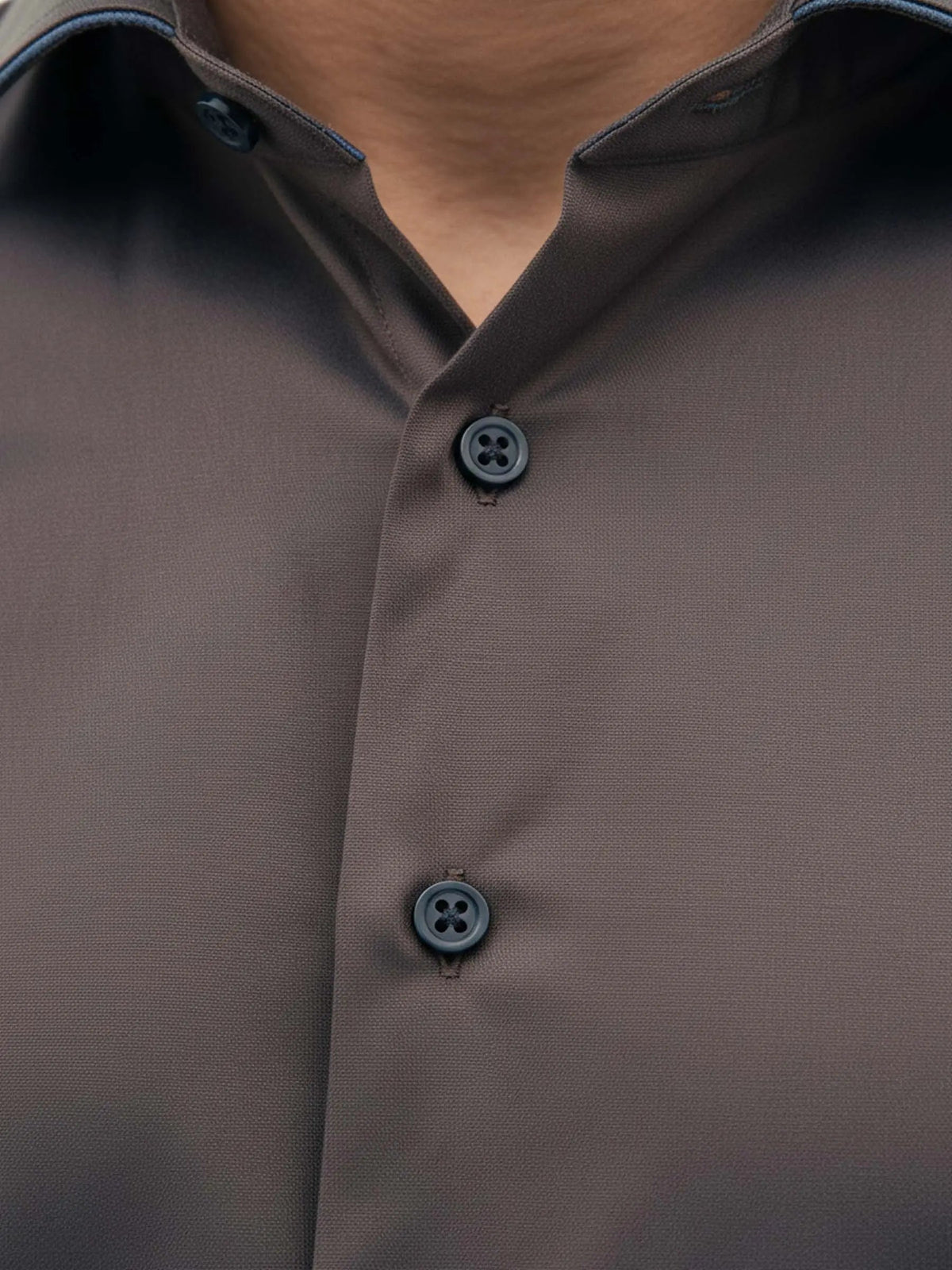 Detail view of light brown men’s shirt with contrast buttons and modern collar.