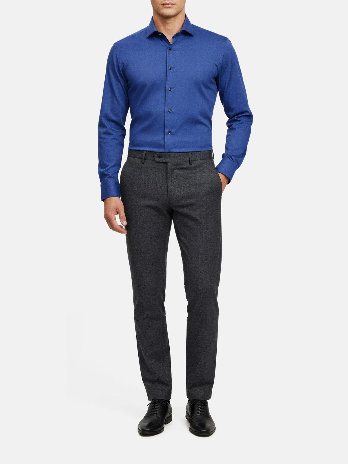 Full-body view of a man wearing a royal blue dress shirt with dark trousers.