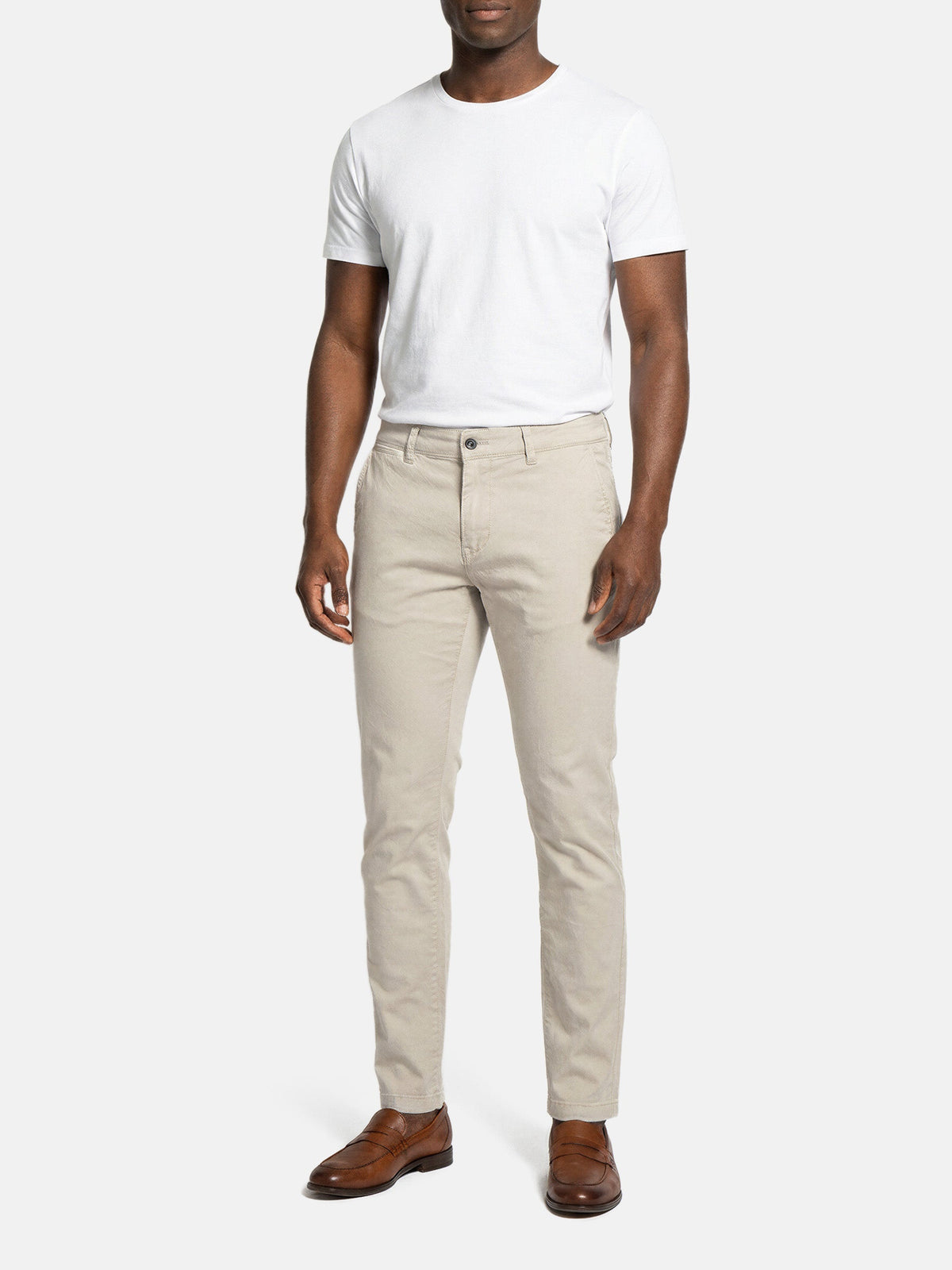 Model wearing light beige slim-fit men’s chino pants styled with white t-shirt.