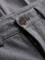Close-up of grey pantalon fabric showing button detail and zip fastening for tailored trousers.