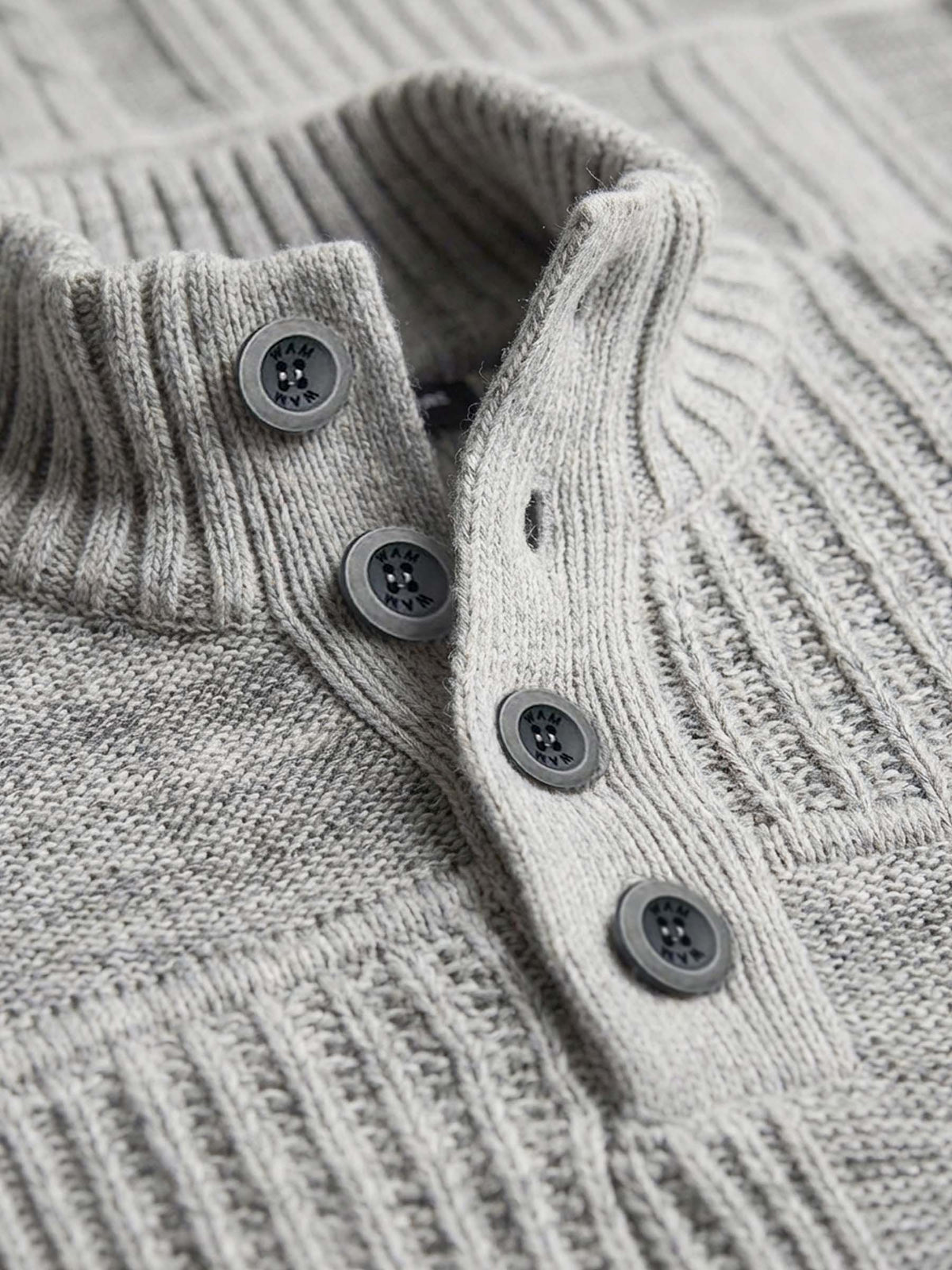 Close-up of light grey knit sweater’s ribbed collar and button placket detailing.