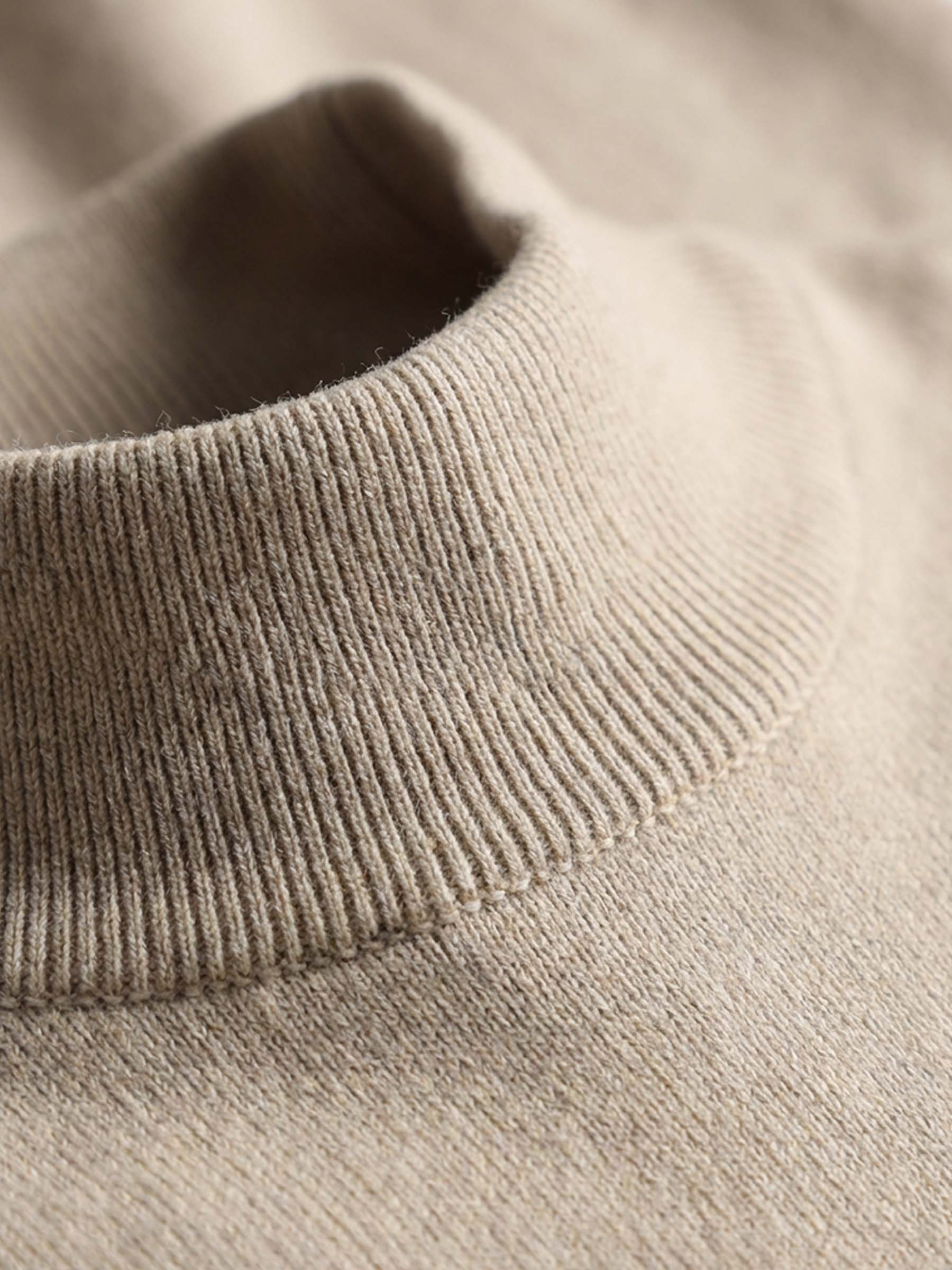 Close-up of beige pullover’s ribbed mock-neck fabric texture.