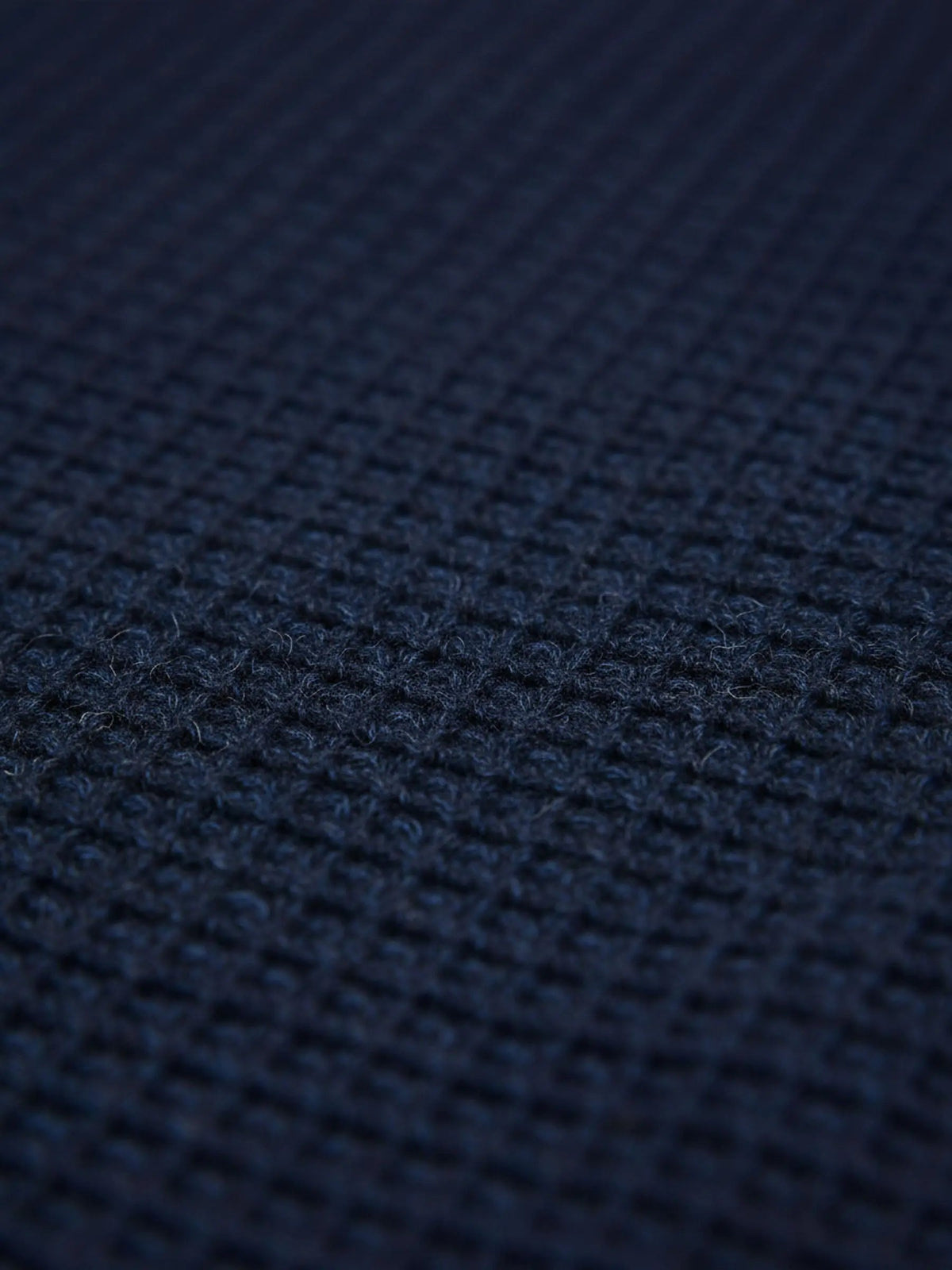 Close-up of indigo navy knit fabric showing dense textured waffle pattern.