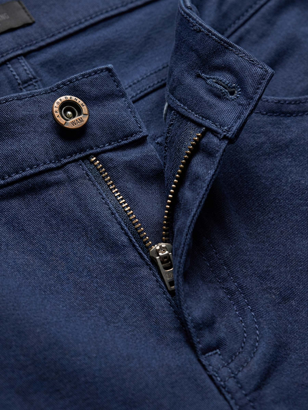 Detail of navy denim jeans with branded button, zipper, and reinforced stitching