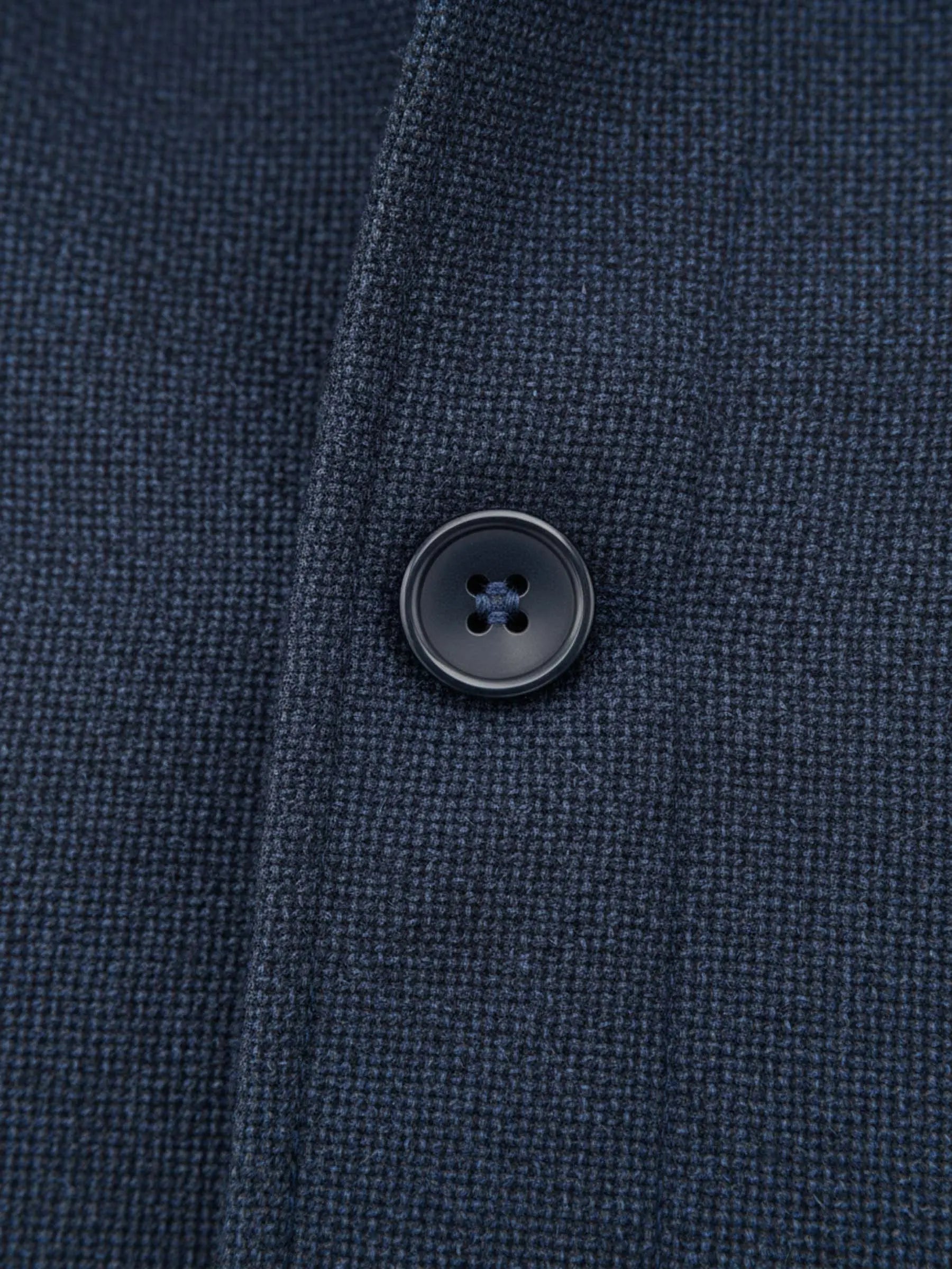Close-up of light navy trenchcoat fabric showing textured weave and black button detail.