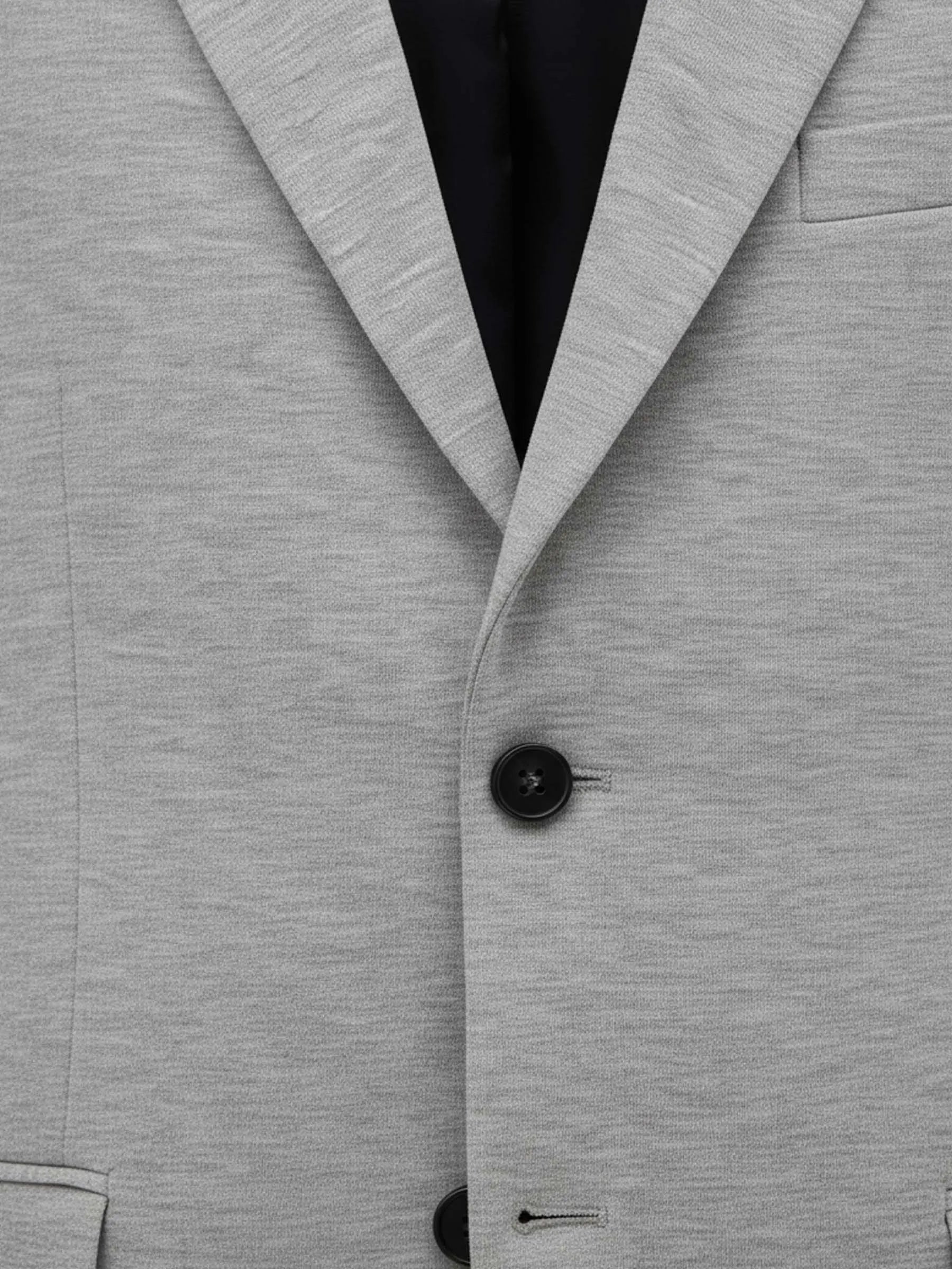 Close-up of light grey blazer fabric and black button details.