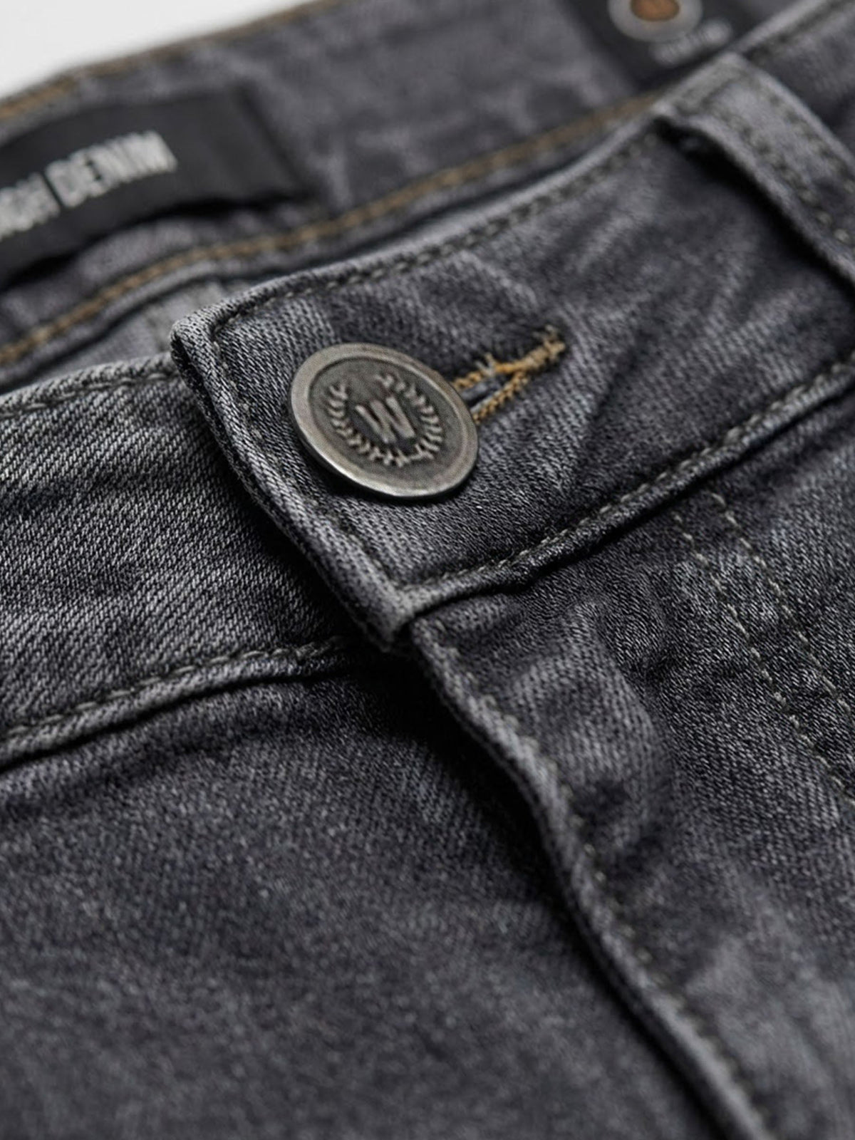 Close-up of grey denim jeans button and waistband stitching detail.