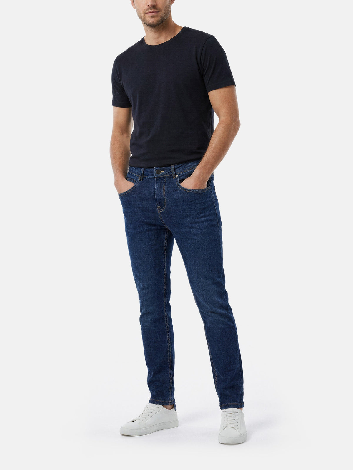 Model wearing blue slim fit jeans styled with black t-shirt and sneakers